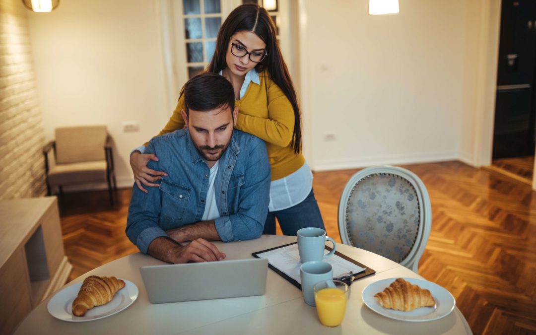 man looking at a computer with a woman standing behind him looking over his should at the same laptop