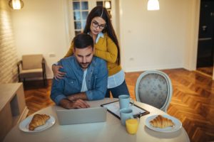 man looking at a computer with a woman standing behind him looking over his should at the same laptop