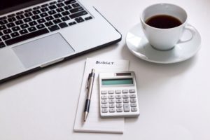 desk with calculator, laptop, coffee, pen, and notepad with the word "budget" on it